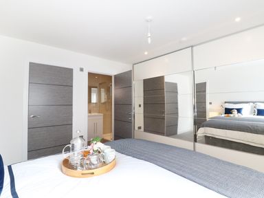 A bedroom with a bed and a tray of tea items with mirrored wardrobes and an open door to a bathroom at An Drowes in Newquay