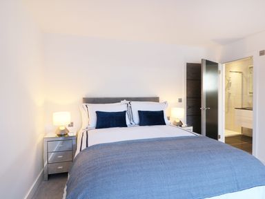 A bedroom with a bed two bedside tables with lamps and an open door showing a bathroom at An Drowes in Newquay