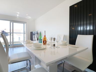 A dining area with a white table set with plates bowls glasses and bottles and white chairs at An Drowes in Newquay