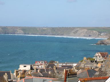 A coastal view with rooftops in the foreground and cliffs across the water at An Drowes in Newquay