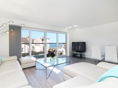 A living room with white sofas glass coffee table and TV near large windows at An Drowes in Newquay