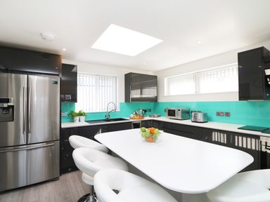 A modern kitchen with stainless steel fridge white island and stools and turquoise backsplash at An Drowes in Newquay