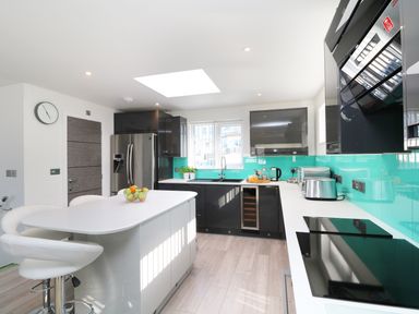A kitchen with an island and two white chairs a fridge and black cabinets with a turquoise backsplash at An Drowes in Newquay