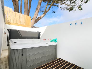 An outdoor hot tub with glasses and towels on the edge in a small fenced area with trees visible beyond the fence at An Drowes in Newquay