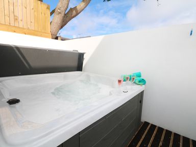 An outdoor hot tub with water and three glasses of pink drink and two rolled towels on the edge at An Drowes in Newquay
