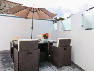 An outdoor dining area with a table chairs an umbrella and a flower pot at An Drowes in Newquay