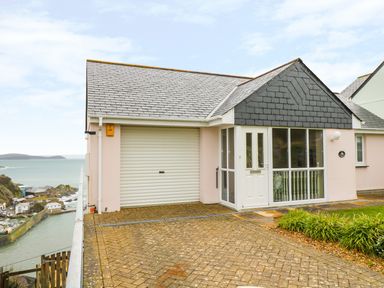 A house with a garage door and a white entrance door overlooking a coastal area at Pink House in Mevagissey