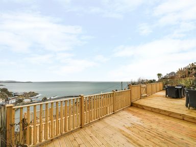 An outdoor wooden deck with a railing and patio furniture overlooking the sea at Pink House in Mevagissey