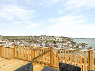 A wooden deck with railing overlooking a coastal town and sea at Pink House in Mevagissey