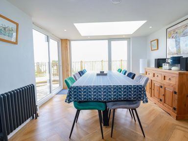 A dining room with a long table covered with a blue patterned tablecloth surrounded by chairs and a wooden sideboard at Pink House in Mevagissey