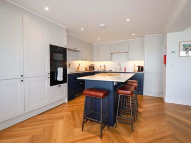 A kitchen with an island and stools with brown seats at Pink House in Mevagissey