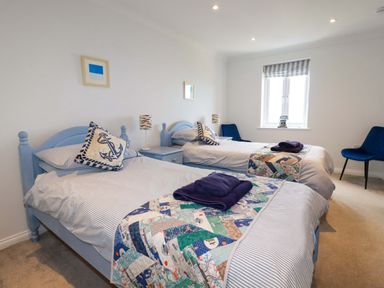 A bedroom with two single beds blue headboards striped bedding patchwork quilts and blue chairs at Pink House in Mevagissey