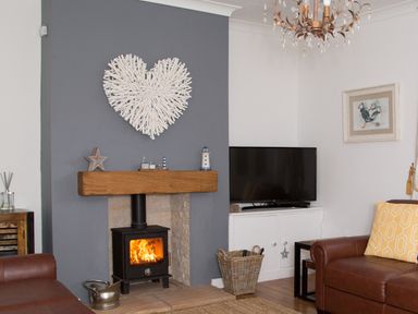 A living room with a fireplace television leather sofas and wall art at Seashell Cottage in Amble-By-The-Sea