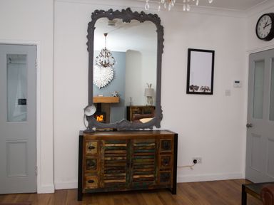 A wooden cabinet with a decorative mirror above and two grey doors on either side at Seashell Cottage in Amble-By-The-Sea
