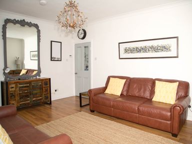 A living room with brown leather sofas yellow pillows a large mirror on a wooden cabinet and a chandelier at Seashell Cottage in Amble-By-The-Sea