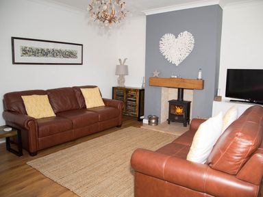 A living room with two brown leather sofas a fireplace and a television at Seashell Cottage in Amble-By-The-Sea