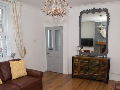 A living room with a brown leather couch yellow pillows a large decorative mirror above a wooden cabinet and a chandelier at Seashell Cottage in Amble-By-The-Sea