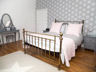 A bedroom with a brass bed frame pink pillows and gray furniture at Seashell Cottage in Amble-By-The-Sea