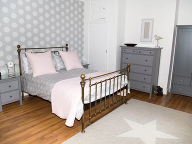 A bedroom with a brass bed frame pink pillows and gray furniture at Seashell Cottage in Amble-By-The-Sea