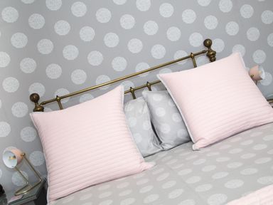 A bed with brass headboard pink pillows and gray bedding with white patterned circles at Seashell Cottage in Amble-By-The-Sea