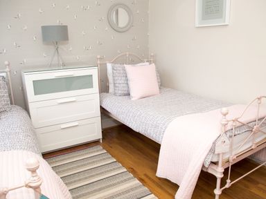 A bedroom with two single beds a white chest of drawers a lamp and bird patterned wallpaper at Seashell Cottage in Amble-By-The-Sea