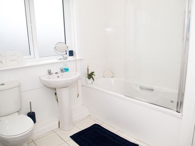 A bathroom with a toilet sink bathtub and a window with decorations at Seashell Cottage in Amble-By-The-Sea