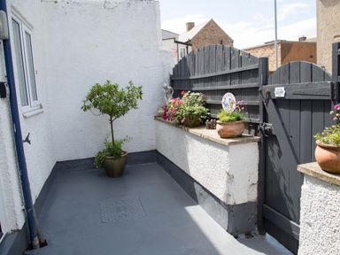 A small outdoor courtyard with potted plants a statue and a black wooden gate at Seashell Cottage in Amble-By-The-Sea