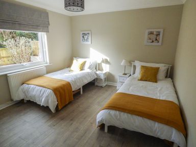 A bedroom with two single beds with white bedding and orange blankets with bedside tables and lamps at Oakdene in Neyland