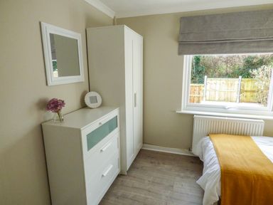 A bedroom with a white chest of drawers a wardrobe a window a bed with a yellow cover and a mirror on the wall at Oakdene Neyland