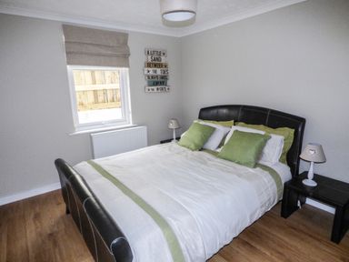 A bedroom with a double bed with green and white bedding two bedside tables with lamps a window with a beige blind and a wall decoration at Oakdene in Neyland