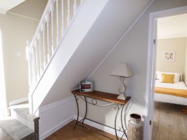 A staircase with carpeted steps next to a wooden table with a lamp and a photo frame near a doorway showing a bedroom at Oakdene in Neyland
