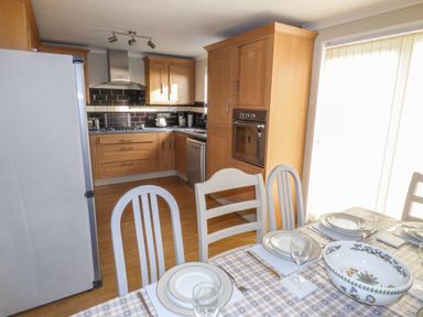 A kitchen and dining area with wooden cabinets a dining table set with plates and glasses at Oakdene in Neyland