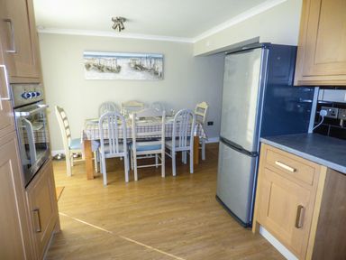 A kitchen with a dining table and chairs fridge and built in oven at Oakdene in Neyland