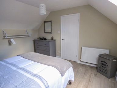 A bedroom with a bed a gray chest of drawers a wall-mounted rack with hangers a white door a radiator and a laundry basket at Oakdene in Neyland