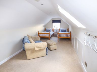A bedroom with two single beds a sofa and an ottoman under a sloping ceiling at Oakdene in Neyland