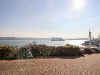 A paved area with bushes overlooking a body of water with a ferry and sailboats at Oakdene in Neyland
