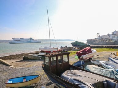 Boats on a shore with a ferry in the water and houses in the background at Oakdene in Neyland