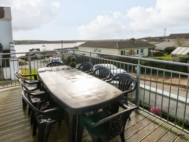 A balcony with a black plastic table and eight matching chairs overlooking houses and a body of water at Oakdene in Neyland