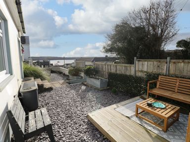 An outdoor patio area with wooden benches and a small table on a rug surrounded by gravel and fenced garden at Oakdene in Neyland