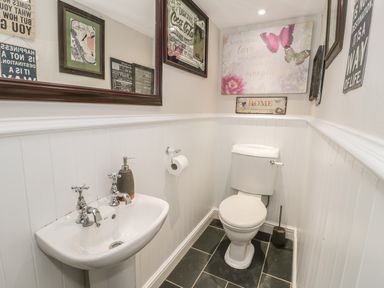 A small bathroom with a toilet and sink and framed pictures on the walls at Plas Mawr in Groeslon