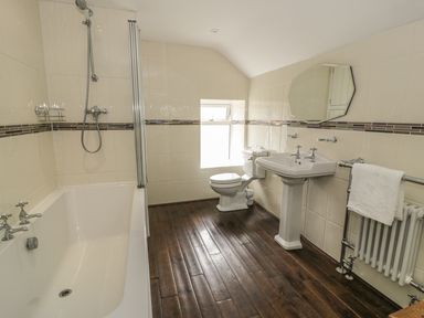 A bathroom with a bathtub shower toilet sink mirror towel on radiator and wooden floor at Plas Mawr in Groeslon