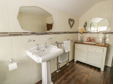 A bathroom with a pedestal sink two mirrors a cabinet with candles and towel rail at Plas Mawr in Groeslon