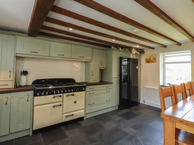 A kitchen with cabinets, stove, refrigerator, and dining table at Plas Mawr in Groeslon
