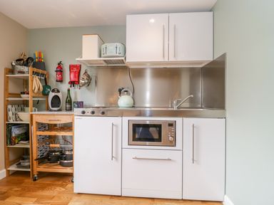 A kitchen area with white cabinets a microwave a kettle a toaster cookware on a wooden shelving unit and a fire extinguisher at Pheasant Lodge in Wimborne Minster