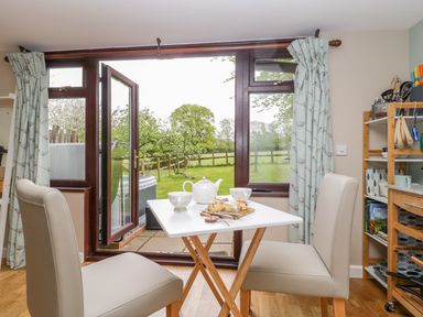 A dining area with a small table set with a teapot cups and scones two chairs and an open door to a garden at Pheasant Lodge in Wimborne Minster