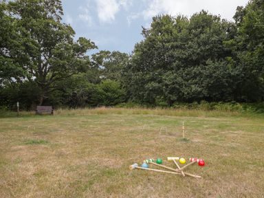 An outdoor grass field with croquet equipment and a bench near trees at Pheasant Lodge in Wimborne Minster