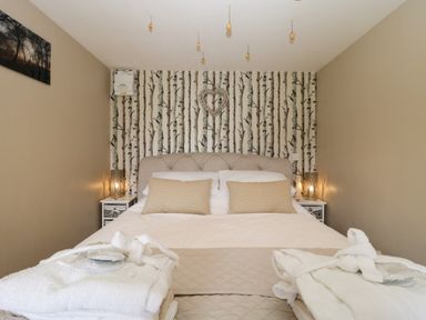 A bedroom with a bed beige pillows bedside tables and lamps at Pheasant Lodge in Wimborne Minster