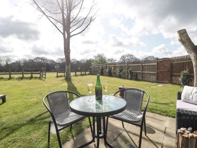 A garden with a round glass table and two chairs with drinks on the table at Pheasant Lodge in Wimborne Minster