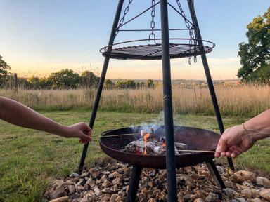 Two people roasting marshmallows over a firepit in a grassy outdoor area at Pheasant Lodge in Wimborne Minster