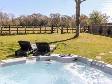 An outdoor hot tub with two lounge chairs on grass near a tree and a wooden fence at Pheasant Lodge in Wimborne Minster
